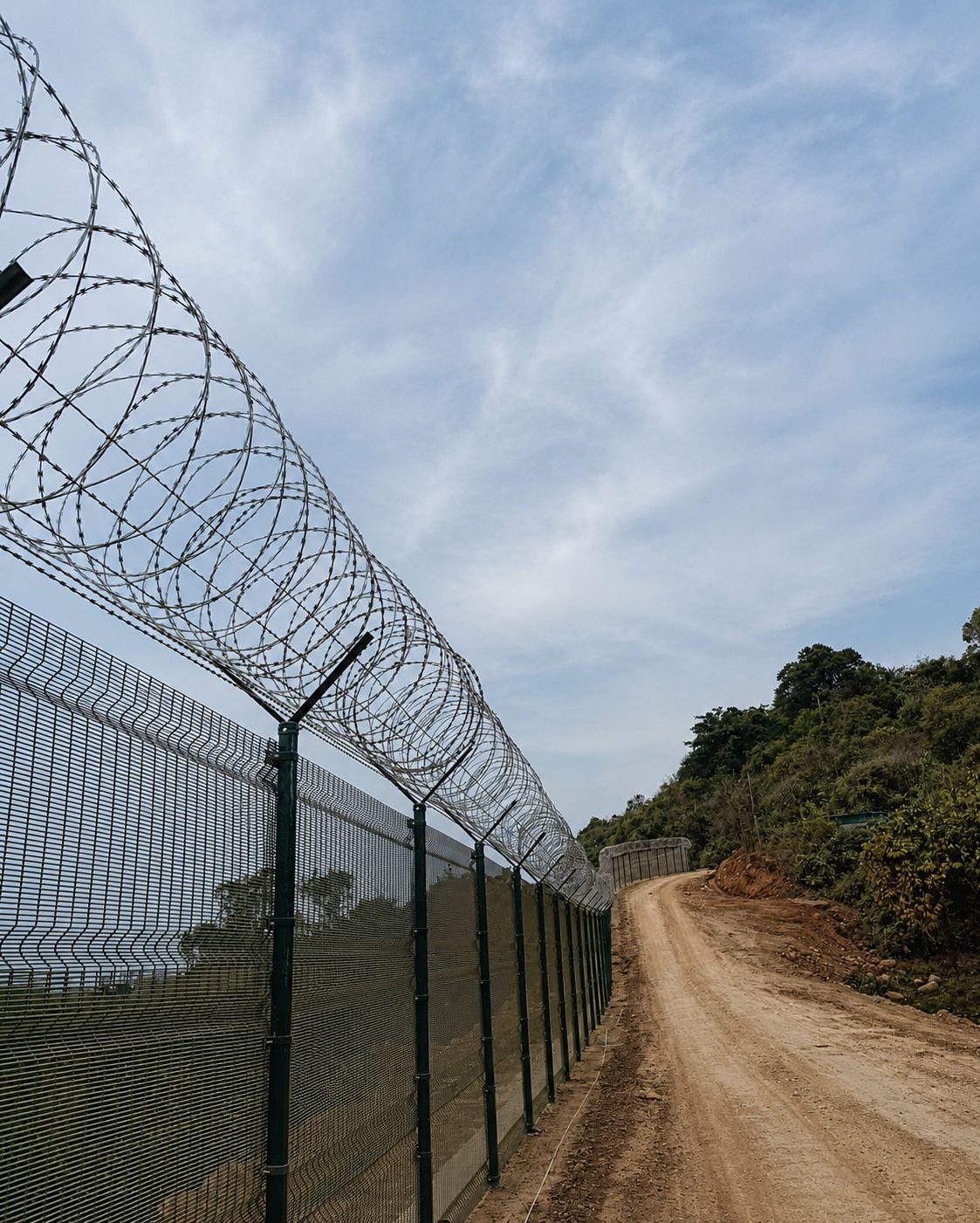 358 anti-climb security fence with concertina coil on hilly terrain